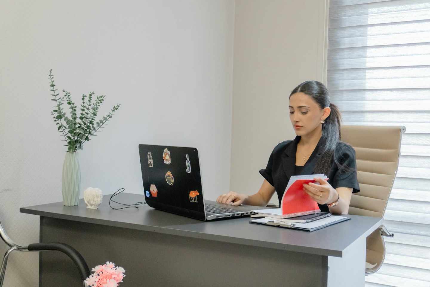 Woman types on laptop at a desk with a red folder.