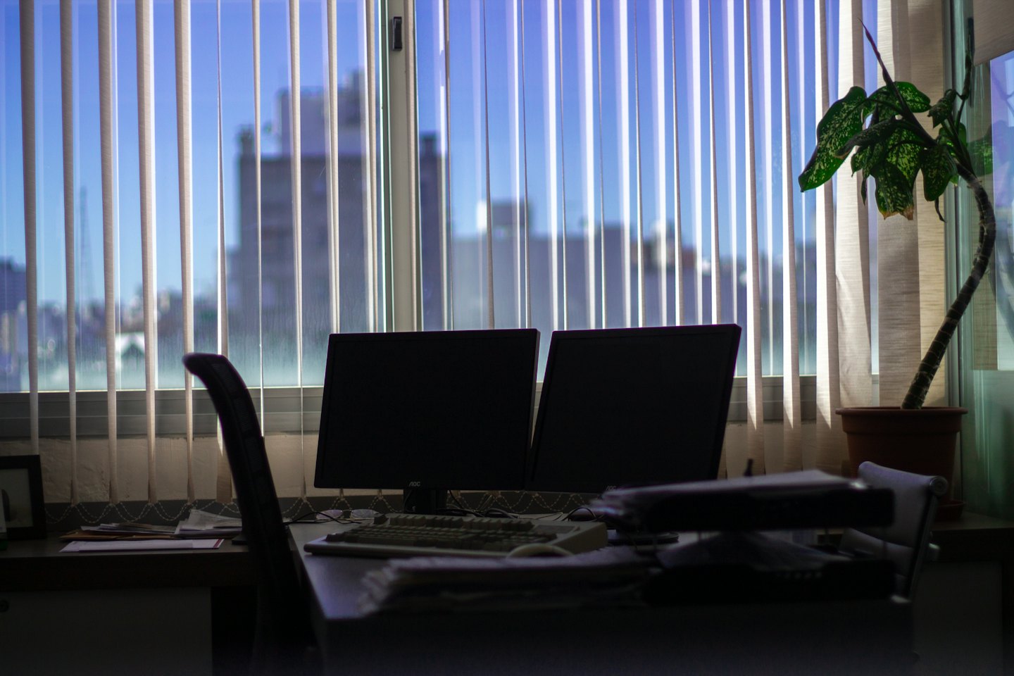 Office desk with computers and papers by a window.